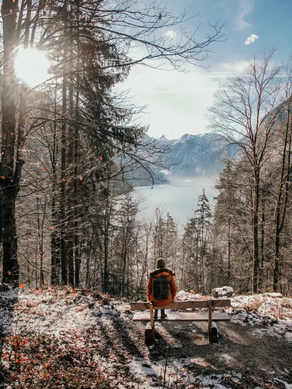 Winter in Ruhpolding Er zit iemand op een bankje met uitzicht op een meer in een winters landschap.