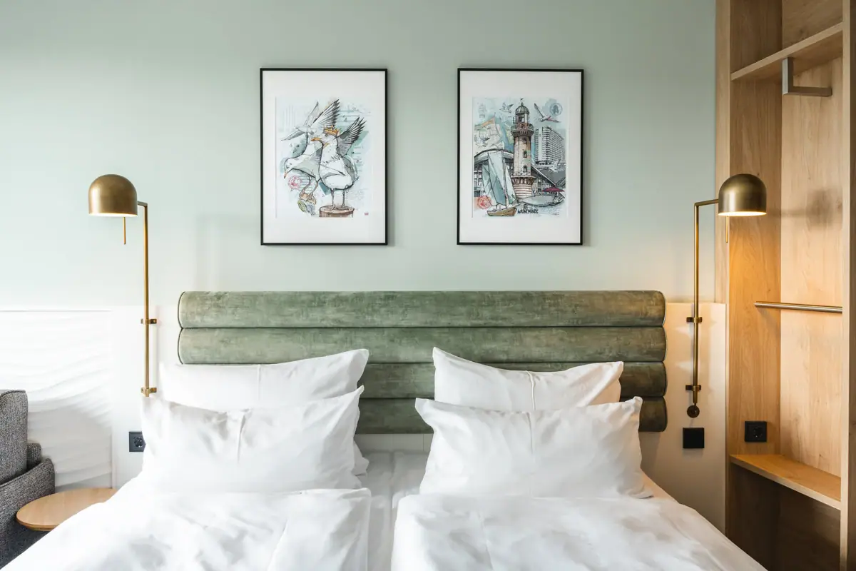 Bed met witte kussens en groen hoofdeinde, geflankeerd door twee lampen.