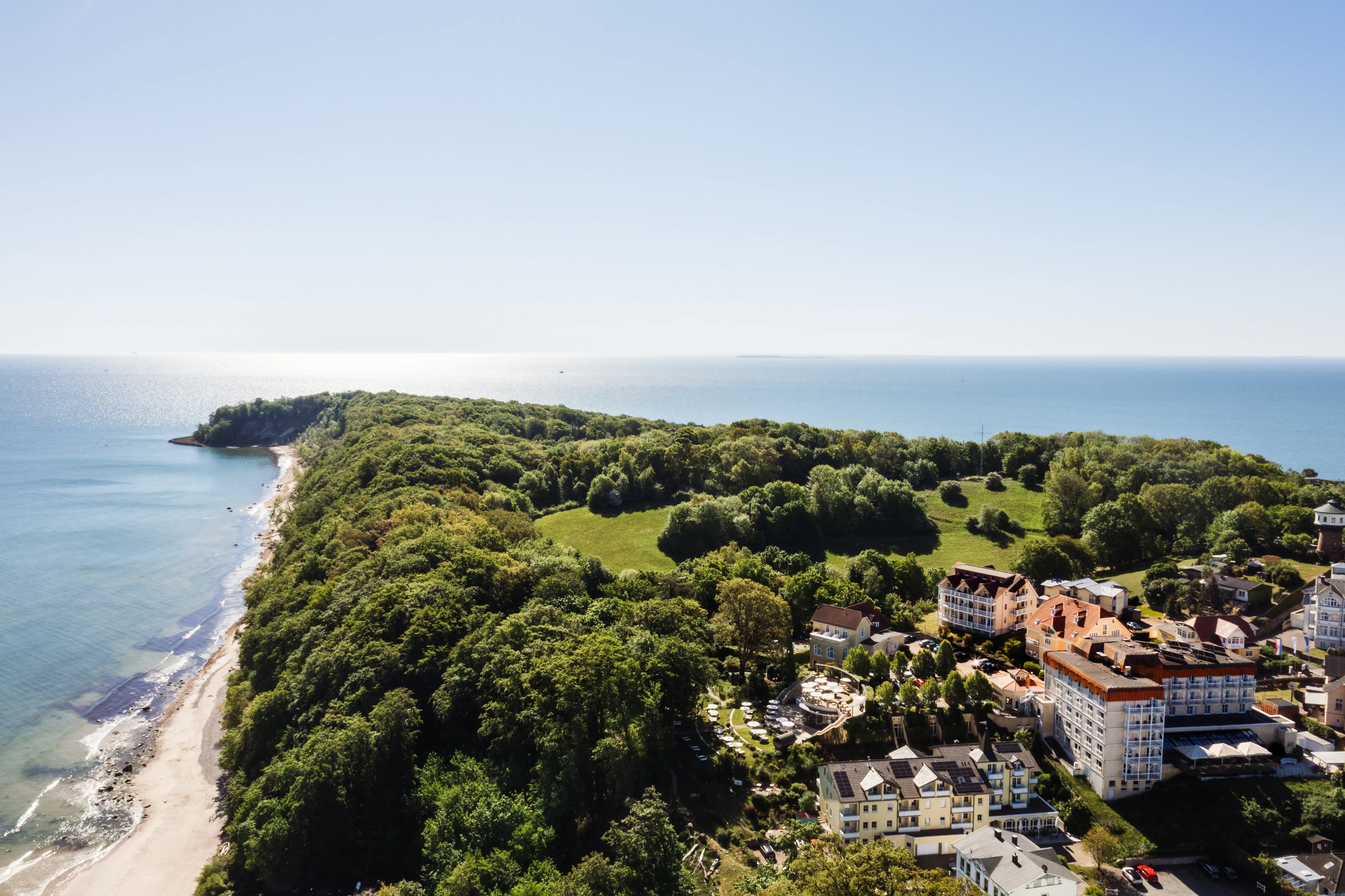 aja Nordperd & Villa's Landschap met bomen en gebouwen, kustlijn en zee op de achtergrond.