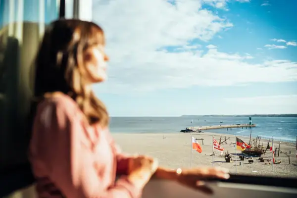 Ausblick Eine Frau blickt aus einem Fenster auf einen Strand.