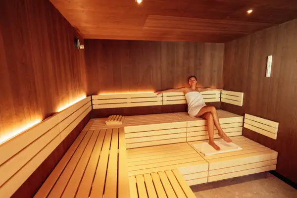 Een vrouw, gewikkeld in een handdoek, zit op een bankje in een sauna.