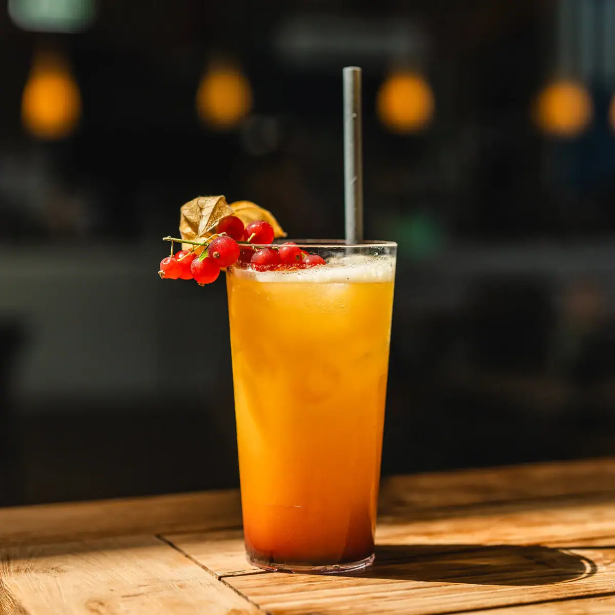 Een glas met een oranje-gele drank, een rietje en bessen.