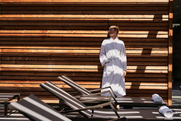Eine Frau in einem weißen Bademantel steht vor einer Holzwand.