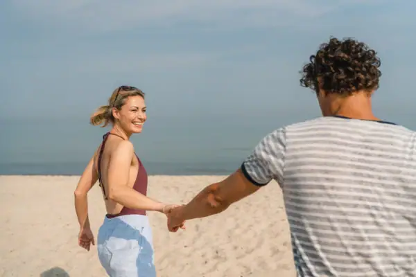 aja biedt Een man en een vrouw houden elkaars hand vast op een strand.