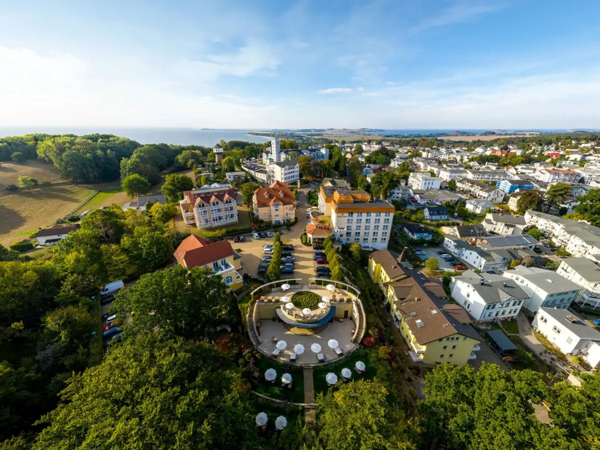 Luchtfoto van een hotel met verschillende huizen met bomen en de zee op de achtergrond.