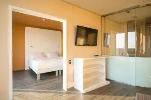 Suite bij de aja Warnemünde Een slaapkamer met een bed en een televisie en een tweede kamer met toegang tot de badkamer.