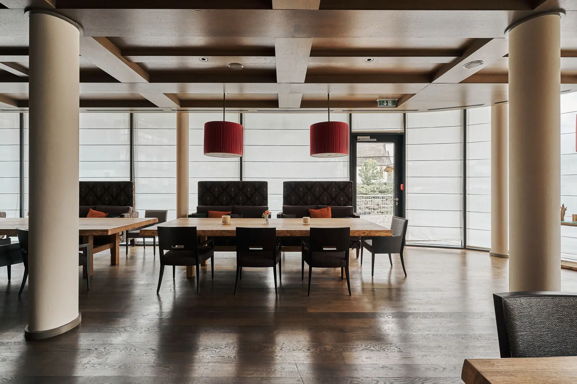 Alpentijd Een grote kamer met een houten vloer, grote tafels en rode lampen. De ramen rondom de kamer zijn bedekt met privacyschermen.