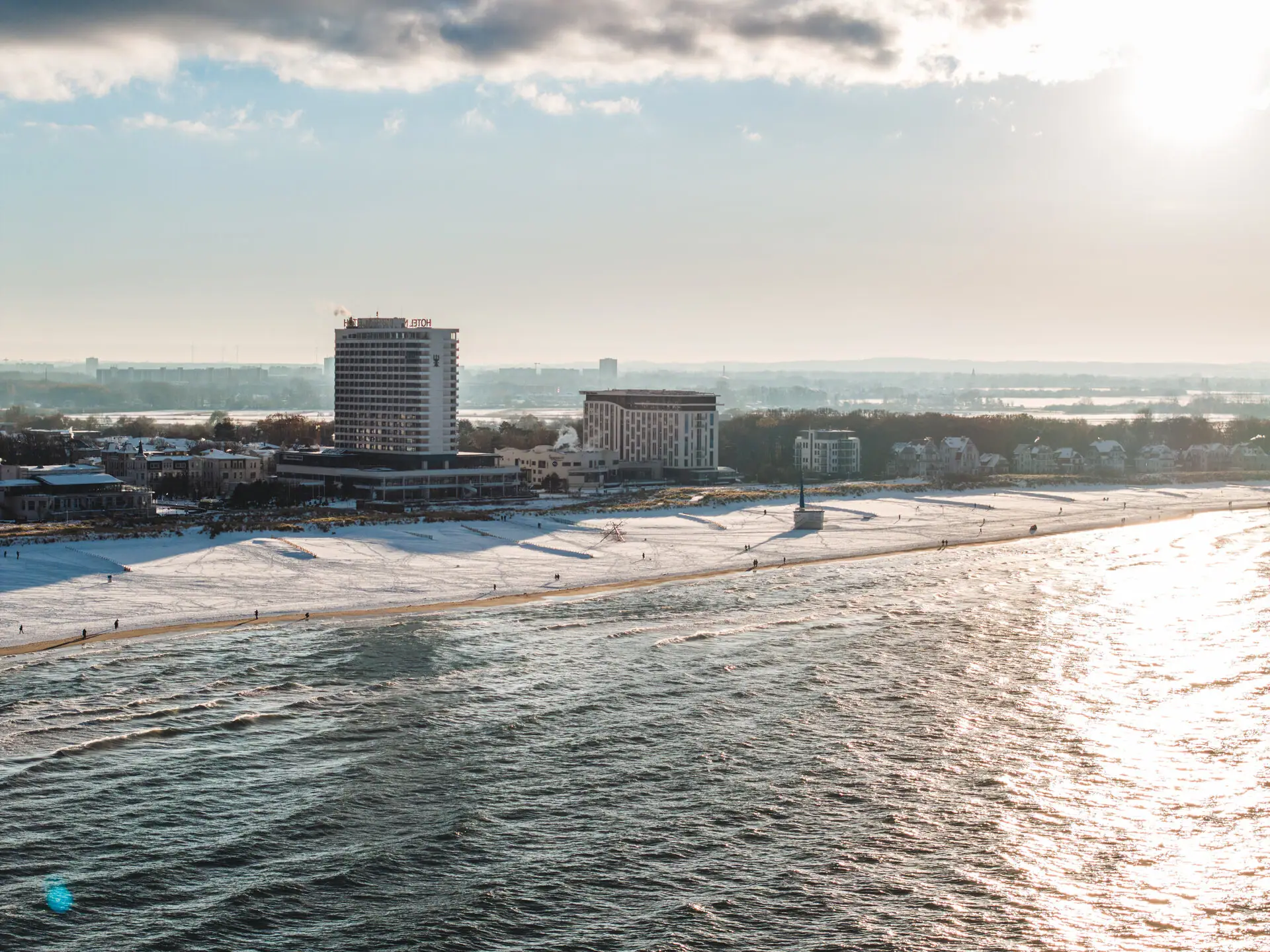 Strand mit dem aja Warnemünde und Schnee im Vordergrund, bewölkter Himmel im Hintergrund.