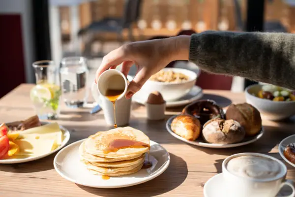 Eén persoon giet stroop op een stapel pannenkoeken.