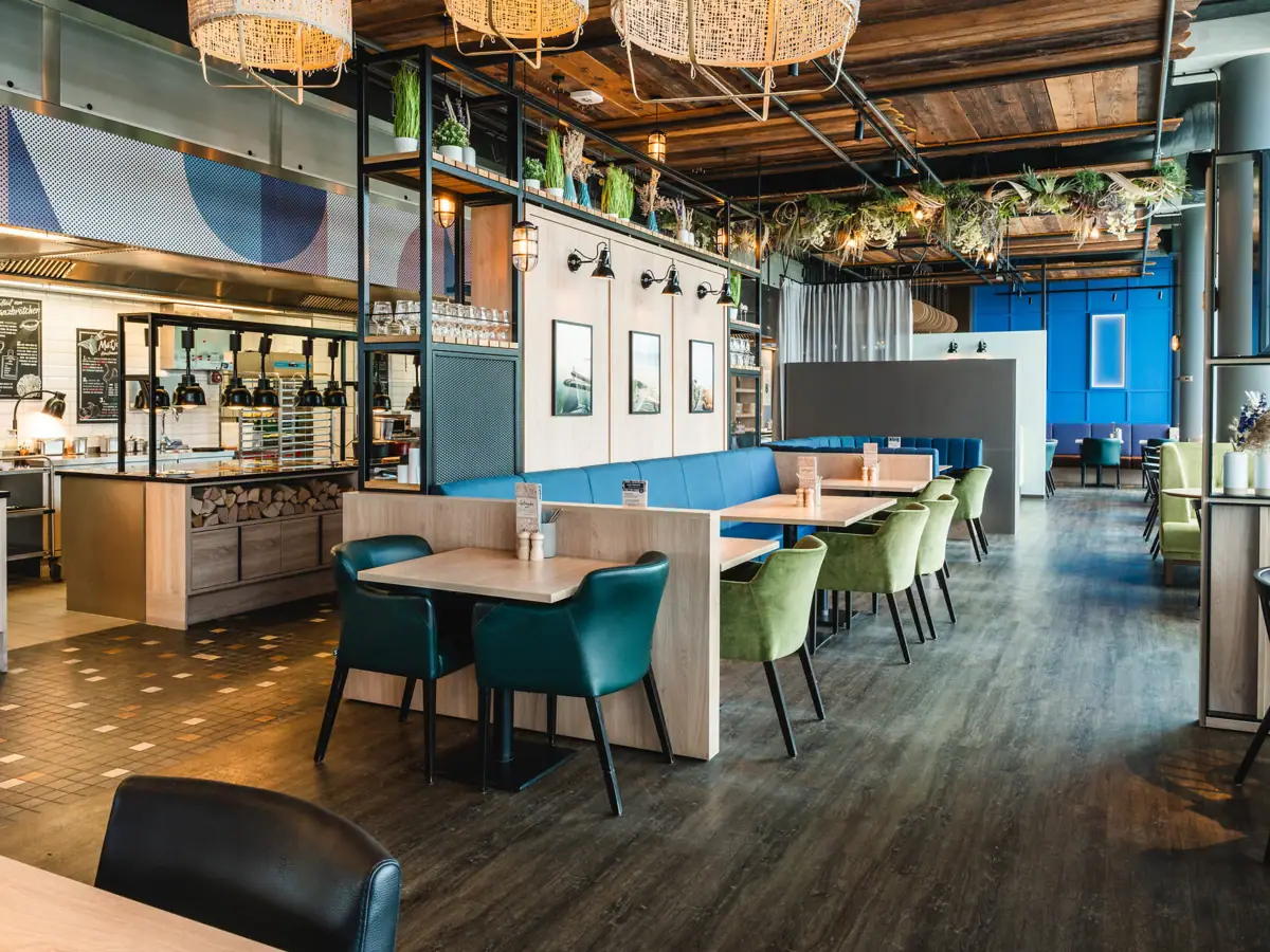 Restaurant bij aja Warnemünde Een restaurant met tafels en stoelen. Stijlvol en modern ingericht. Maritieme uitstraling met foto's van Warnemünde aan de muur. Open buffetruimte op de achtergrond.