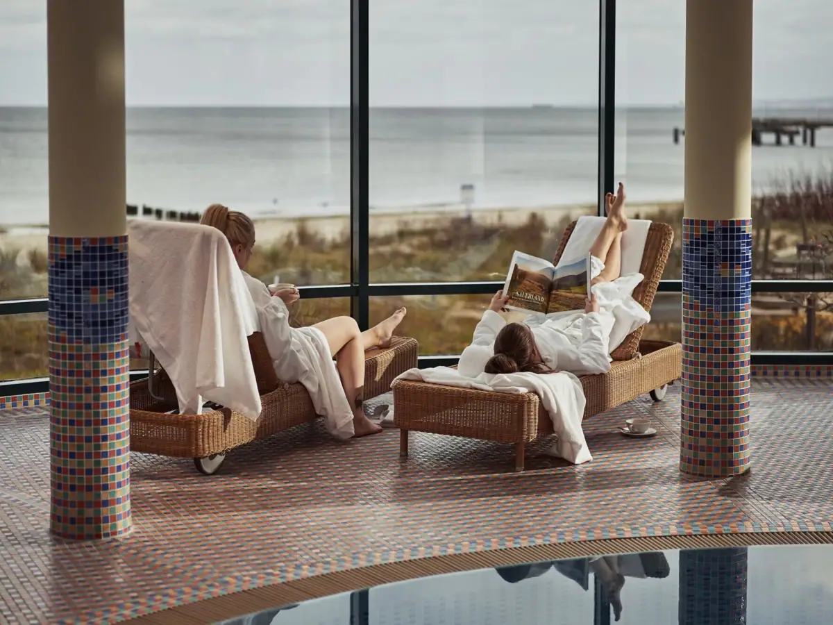 Een groep vrouwen in witte gewaden ligt op stoelen bij het zwembad.