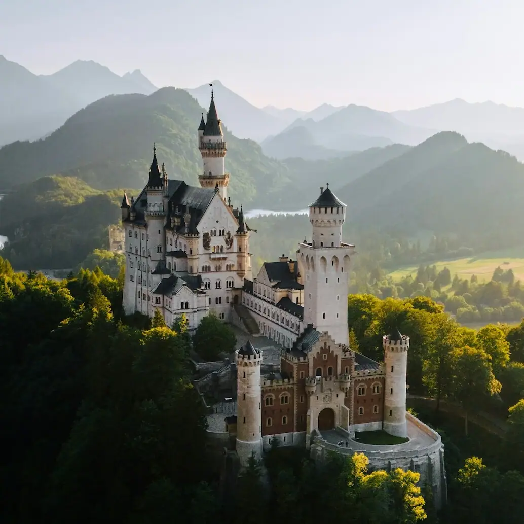 Kasteel Neuschwanstein op een heuvel met bomen en bergen op de achtergrond.