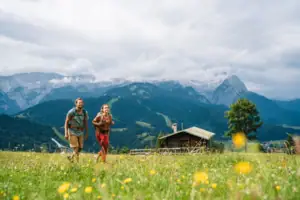 Wandern Garmisch Ein Mann und eine Frau gehen in einem Feld mit Bergen im Hintergrund.